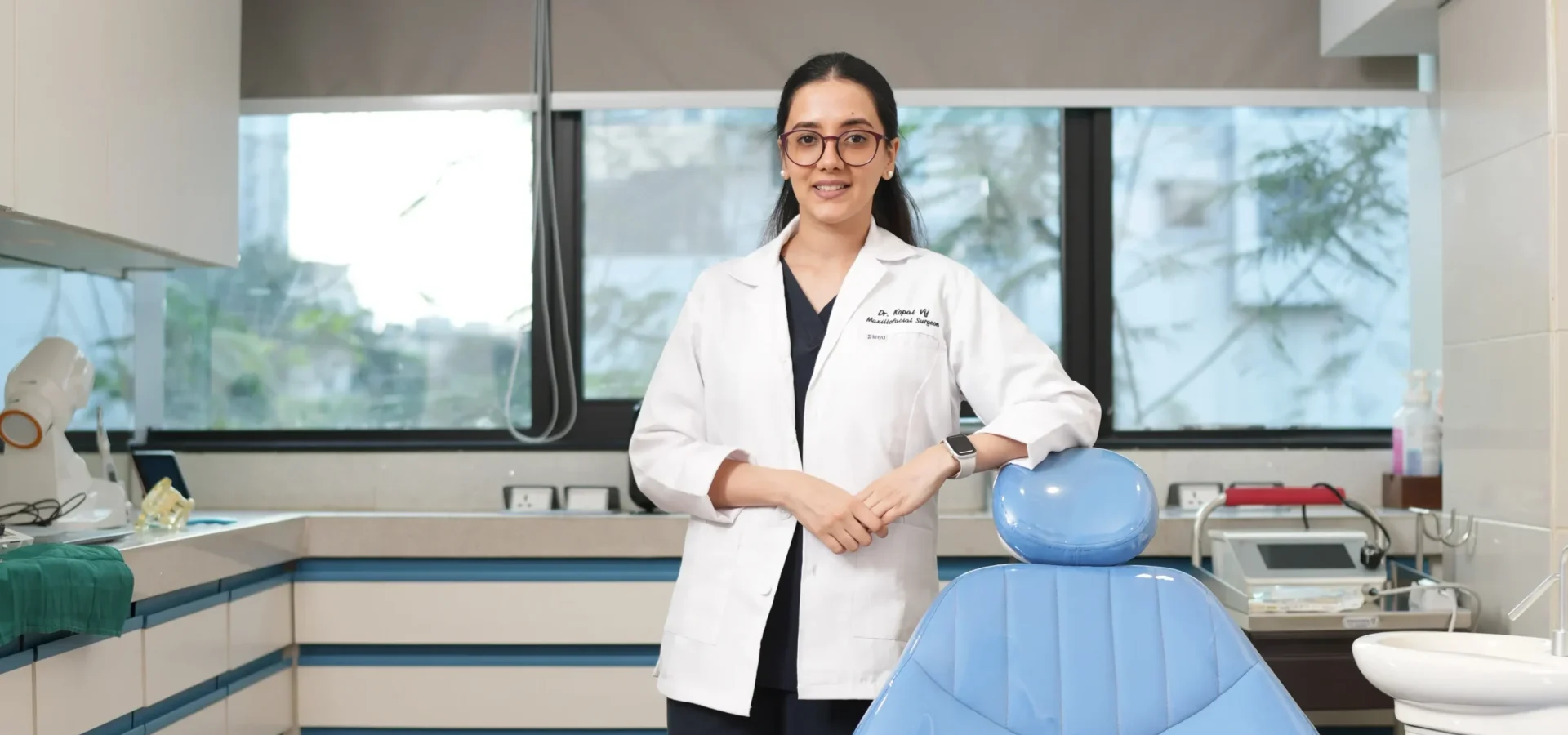 Dr. Kopal Vij - Expert Dentist at Casa Dentique Seawoods Navi Mumbai Dr. Kopal Vij, professional dentist in white coat at Casa Dentique modern dental clinic in Seawoods, Navi Mumbai, standing beside dental chair in well-equipped treatment room